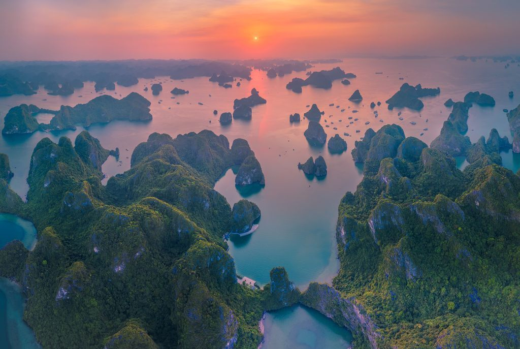 A vibrant sunset over Ha Long Bay, casting a golden glow on the water and the surrounding islands.