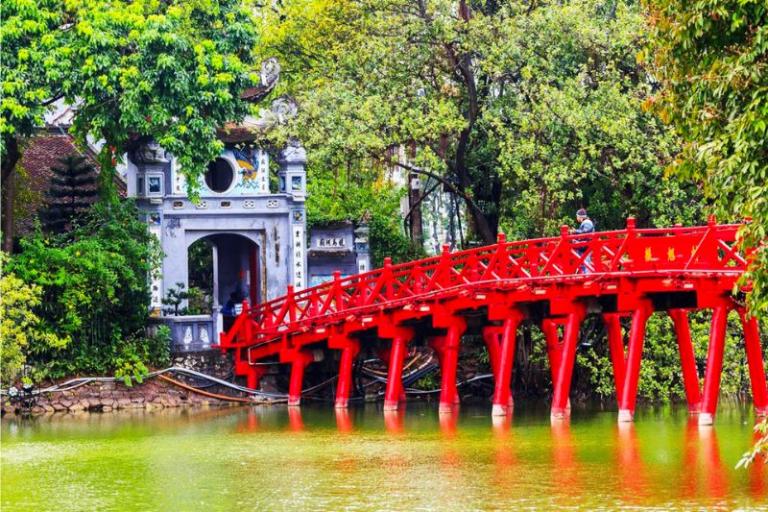 The Huc Bridge, an elegant scarlet-painted wooden bridge that gracefully arches over the water.