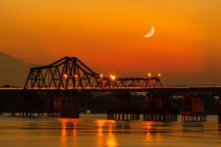 Long Bien Bridge at night: a serene beauty, its lights reflecting over the Red River's gentle flow.