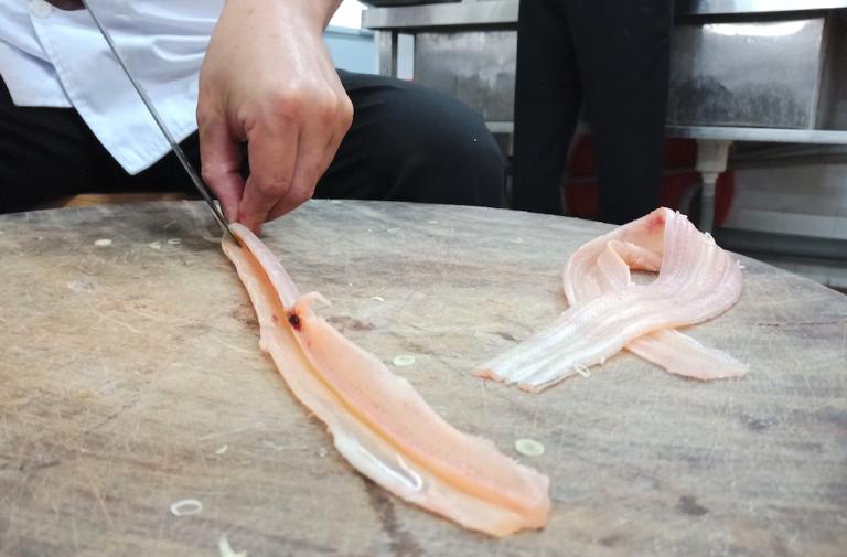 Nhech fish is cleaned with salt and vinegar, deboned, and thinly sliced for preparation.