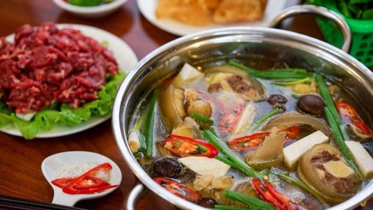 Lau De, or goat hotpot, offers a rich broth, tender goat meat, and fresh vegetables for a hearty meal.