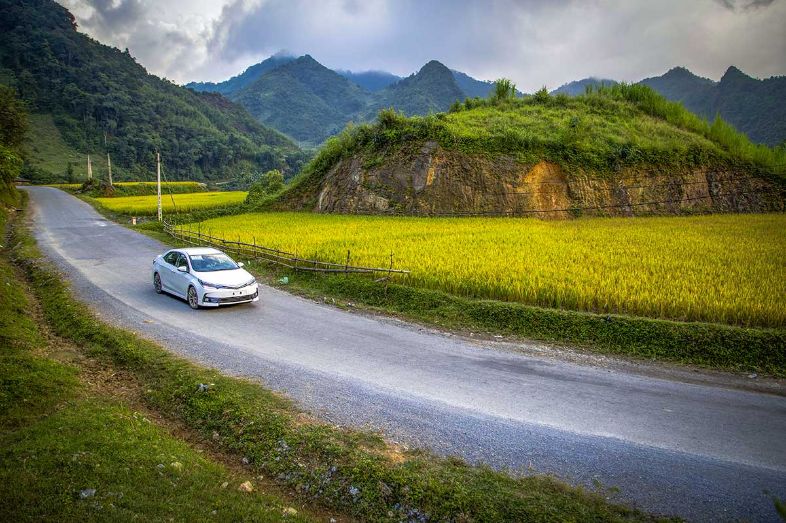 A private car or taxi driving along a scenic road towards Cao Bằng, Vietnam, surrounded by mountains and greenery.