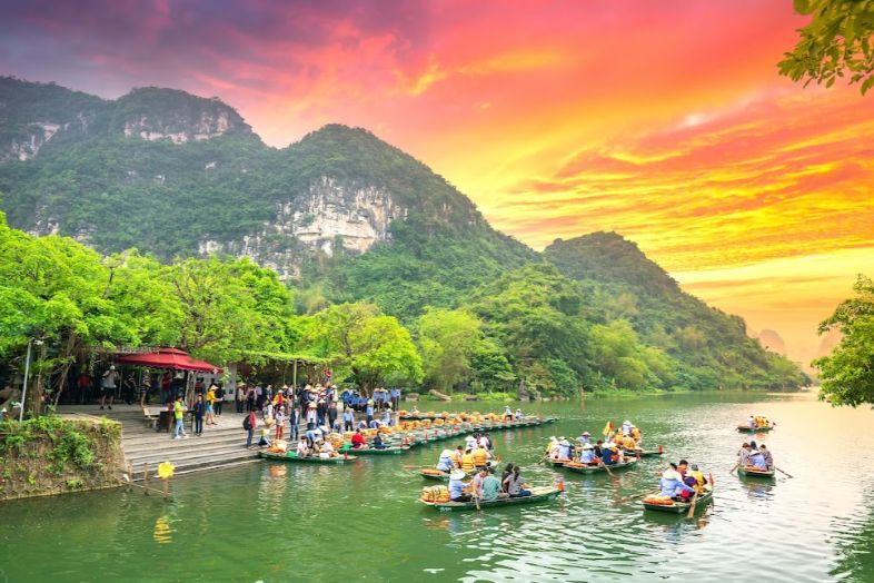 Boats gliding along Tam Coc’s river with limestone karsts and rice fields, and Bích Động Pagoda nestled on a mountainside.