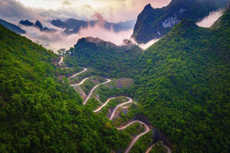 A winding mountain road at Me Pja Pass in Vietnam, surrounded by lush greenery and rolling hills.