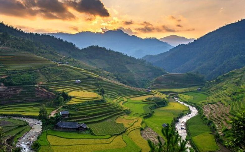 A wide scenic view of Vietnam showing lush mountains, calm water, and soft morning light.