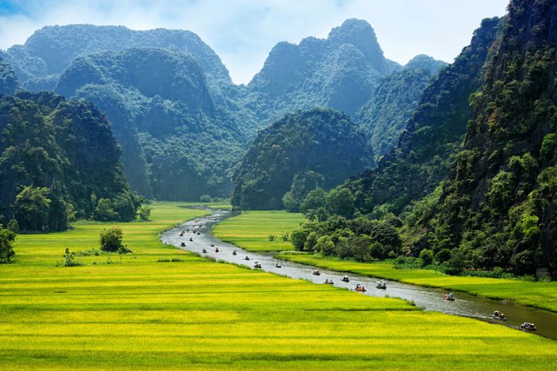 Rowing boat traveling through Tam Coc’s river landscape with limestone mountains and vibrant rice paddies.